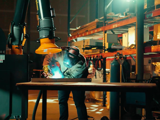 A welder working on a metal project while a Fume Xtractors portable works to extract fumes and smoke.