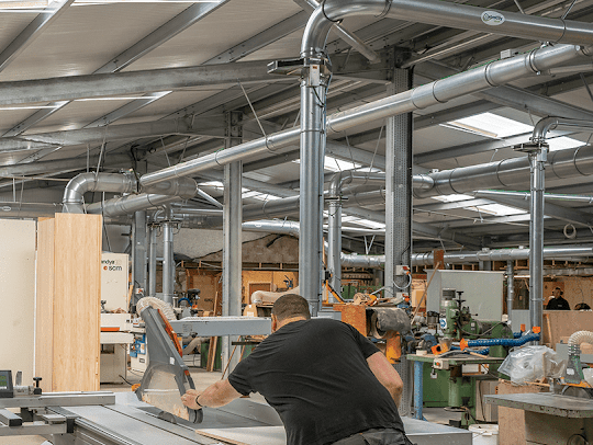 A machine operator working on a wood project in a large woodworking facility with a Nordfab ducting system shown installed and attached to various machinery.